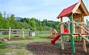 A beautiful playground with a wooden structure, slide, and swings. In the background, green meadows and trees can be seen.