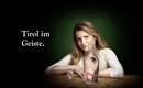 Een vrouw zit aan een tafel, achter een glazen fles met een gezicht. De achtergrond is donkergroen, en de tekst zegt "Tirol in Geest".