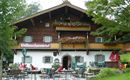 Ein traditionelles Holzhaus mit blühenden Balkonen und einer einladenden Terrasse. Gäste sitzen draußen und genießen die ruhige Umgebung.