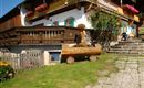 Ein traditionelles alpenländisches Haus mit Balkonen und Blumenkästen. Im Vordergrund befindet sich eine Holzbank und der Weg führt zu den Treppen.