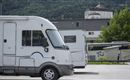 A motorhome is parked in a lot overlooking a mountainous landscape. In the background, a large building can be seen.