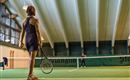 Eine Tennisspielerin steht auf dem Platz und blickt zum Netz. Der Innenbereich ist gut beleuchtet mit einer grünen Spielfläche.