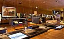 Ein moderner Ausstellungsraum mit verschiedenen Exponaten und Kunstwerken. Die Wände sind aus Holz, und es gibt eine einladende Atmosphäre.