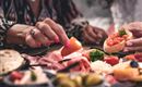 Ein gedeckter Tisch mit verschiedenen italienischen Vorspeisen, darunter Oliven, Schinken und Bruschetta. Zwei Personen genießen das Essen und teilen sich die leckeren Snacks.