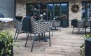 Eine gemütliche Terrasse mit modernen Stühlen und Tischen. Blumen in Töpfen verleihen dem Raum einen einladenden Charakter.