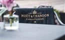 Ein elegantes Tuch mit dem Logo von Moët & Chandon liegt auf einem Stuhl. Im Hintergrund ist eine Vase mit einer Blume zu sehen.