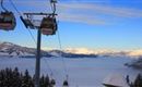 Een kabelbaan rijdt over een met sneeuw bedekt landschap met bergen op de achtergrond. Onder zich verspreidt zich een zee van mist.