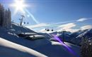 Een schilderachtig winterlandschap met sneeuwbedekte bergen en een heldere blauwe lucht. Skiliften rijden over de besneeuwde piste.