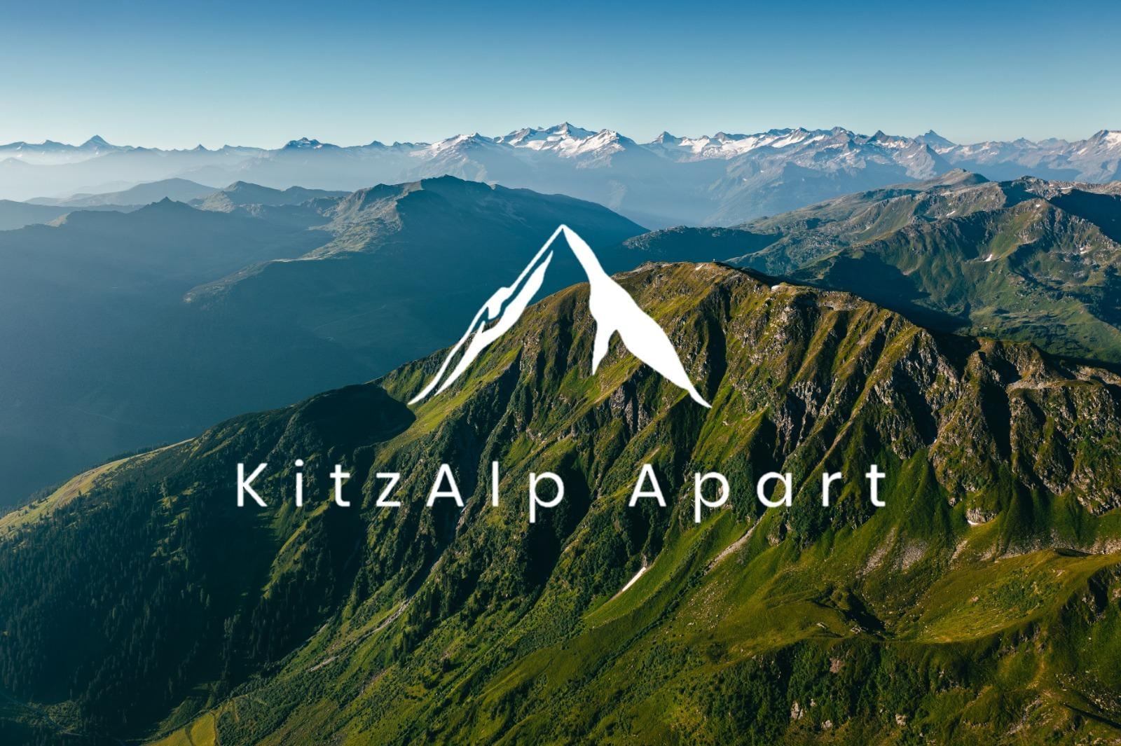 Eine beeindruckende Berglandschaft mit grünen Hügeln und schneebedeckten Gipfeln im Hintergrund. Im Vordergrund steht das Logo von KitzAlp Apart.