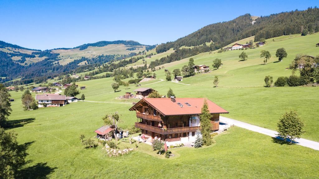 A picturesque landscape with a typical alpine house in the middle. Surrounded by green meadows and gentle hills.