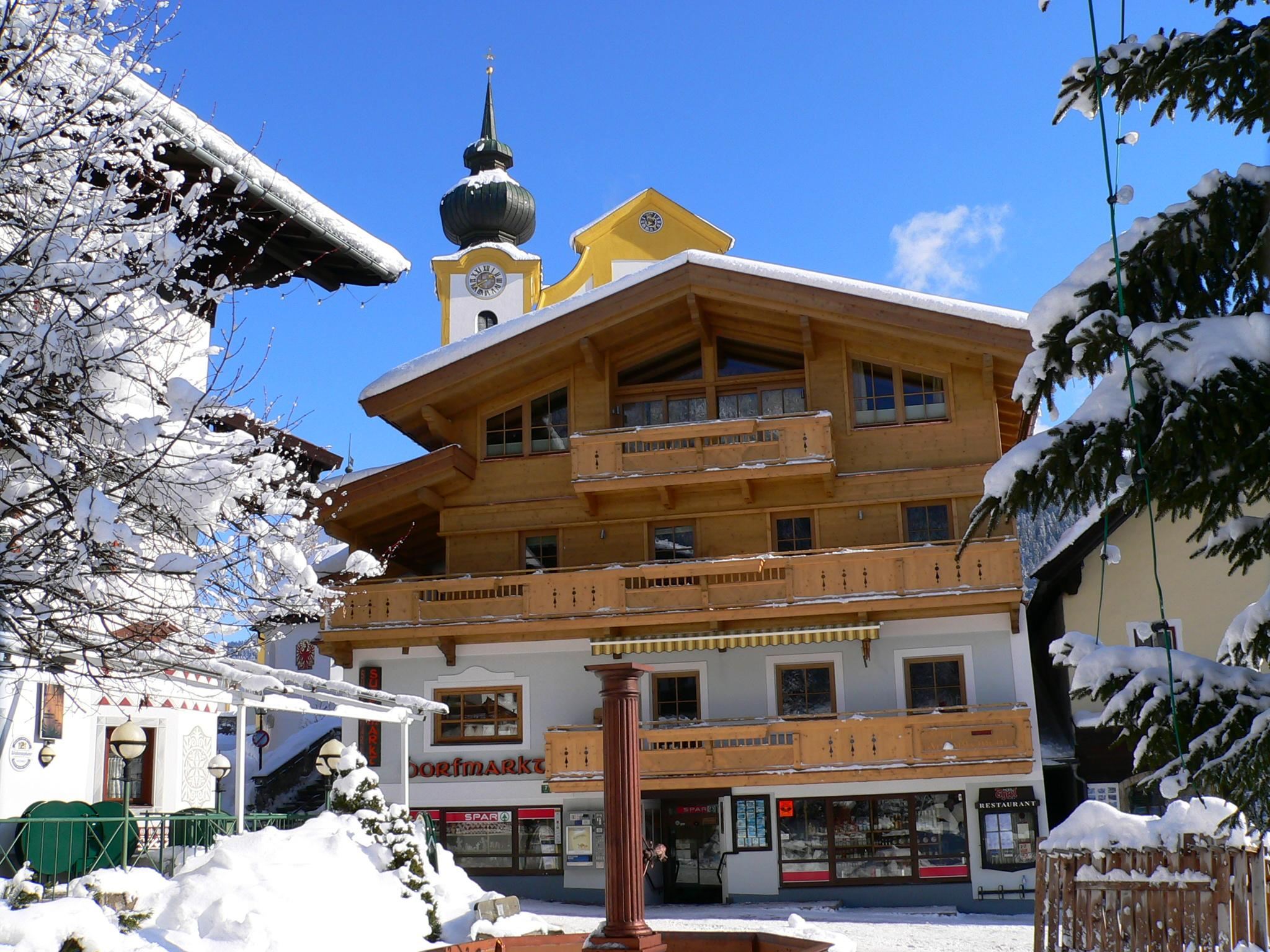 Ein wunderschönes Gebäude im alpinen Stil, umgeben von schneebedeckten Bäumen. Der klare blaue Himmel vervollständigt die winterliche Landschaft.