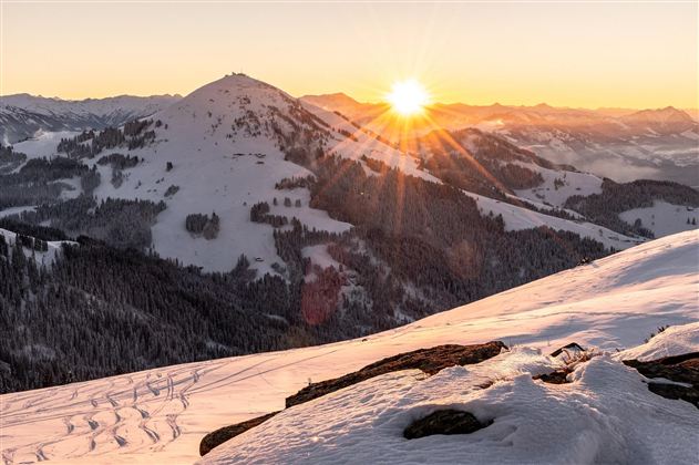 A snowy mountain landscape at sunrise. The sun shines over the mountains and the winter forest.