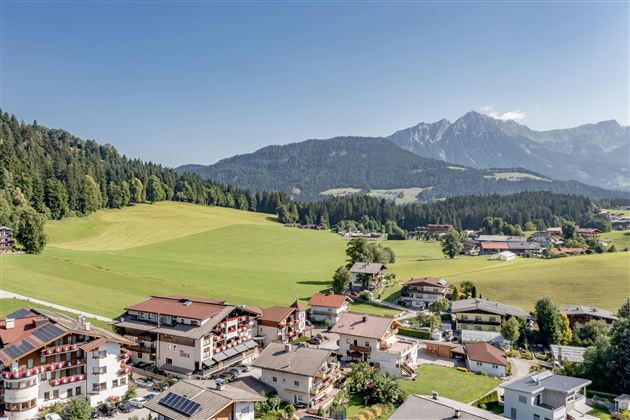 A picturesque village in a green landscape with a view of the mountains. The houses are surrounded by meadows and forests.