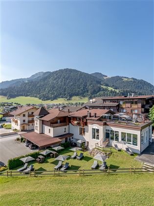 A beautiful hotel amidst a green landscape with mountains in the background. The terraces are equipped with loungers and invite relaxation.