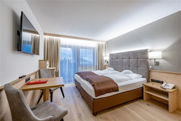 A modern hotel room with a double bed and a cozy seating area. Large windows provide plenty of daylight and offer access to a balcony.