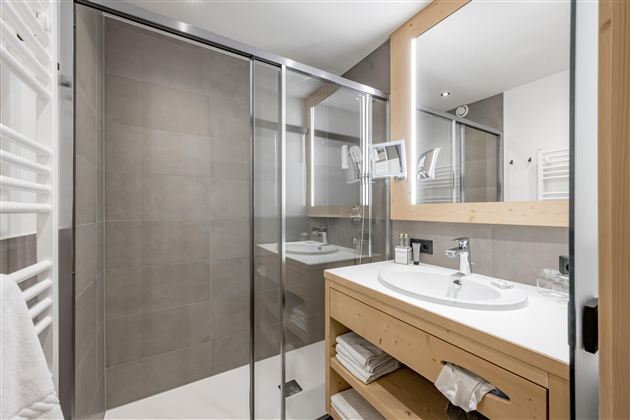 A modern bathroom with a glass shower and a wooden sink. The room is bright and clean with neutral colors.