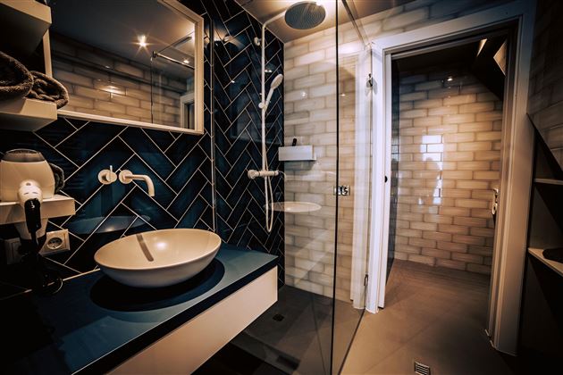 A modern bathroom with blue tiles and an elegant sink. The shower is separated by a glass door, and the room is well lit.