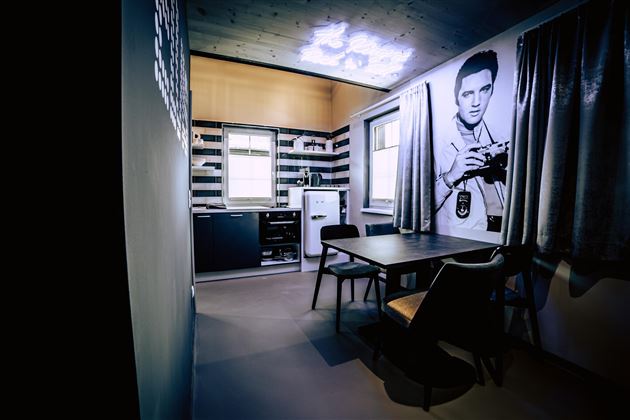 A modern kitchen with a dining table and chairs. On the wall is a large picture of a man with a camera.