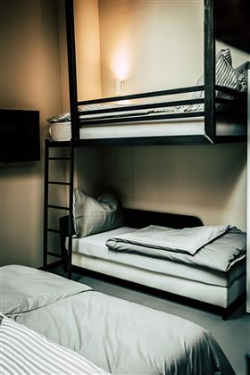 Ein modernes Zimmer mit einem Etagenbett und einem Einzelbett. Die Einrichtung ist schlicht und funktional mit sanfter Beleuchtung.