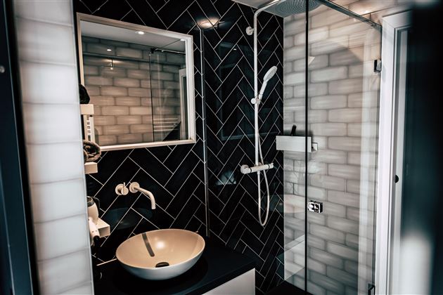 Ein modernes Badezimmer mit schwarzen Fliesen und einer großen Duschkabine. In der Mitte befindet sich ein elegenes Waschbecken.