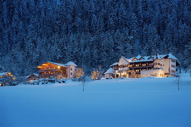 A wintry landscape with snow-covered hills. Cozy houses gently glow in the twilight.