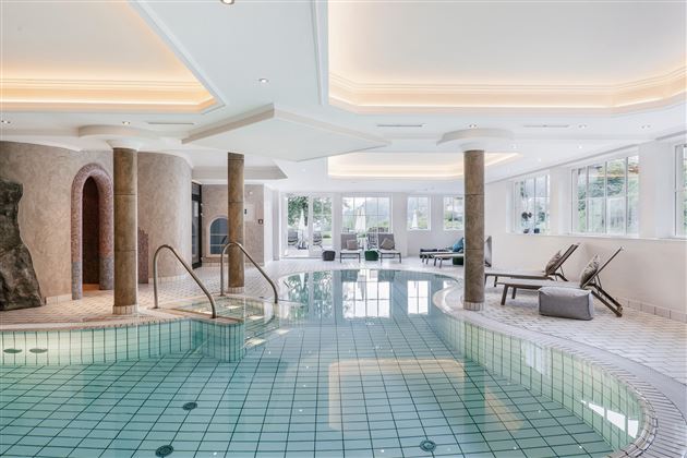 An elegant indoor swimming pool with clear water and modern loungers. The large windows let in plenty of daylight and create a relaxed atmosphere.