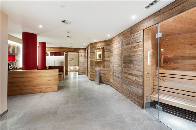 A modern wellness area with natural wooden walls and plain tiles. In the background, a sauna can be seen.