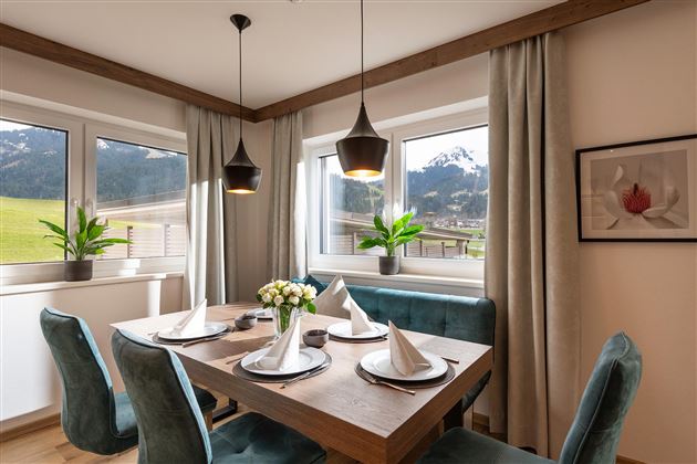 A modern dining room with a wooden table and elegant chairs. Large windows provide a view of the mountains and plenty of daylight.