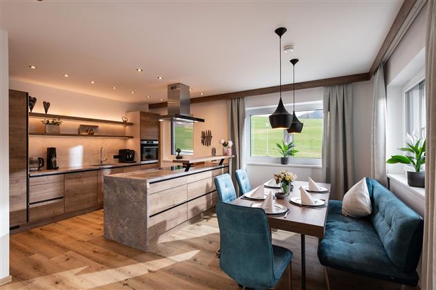 Modern kitchen with wood and stone elements. An inviting dining table with blue chairs and a view of the outdoors.