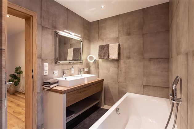 A modern bathroom with a freestanding bathtub and a double sink. The walls are designed in a concrete look, and a large mirror adds style.