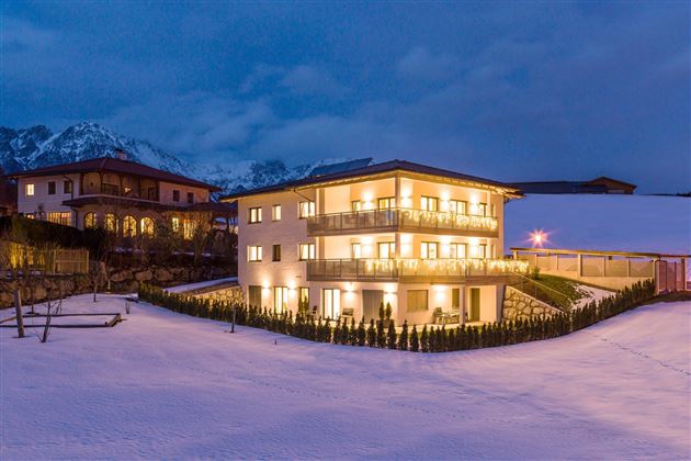 A modern building in the snow, surrounded by mountains. The warm lights illuminate the facade at dusk.