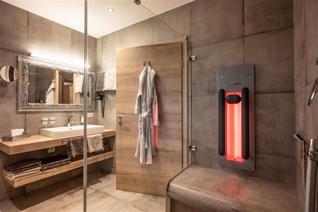 A modern bathroom with wood and concrete elements. There is a sink, a mirror, and an infrared heat lamp.