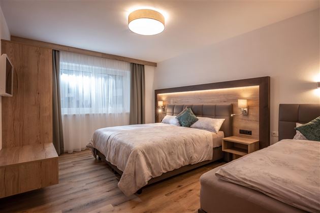 A modern hotel room with two beds and a large window. The decor is elegant and bright with wood and fabric elements.