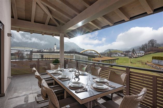 A cozy terrace with a large dining table and a view of the mountains. The surroundings are green and the clouds create a relaxed atmosphere.
