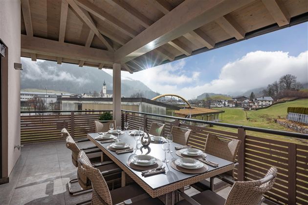 A spacious terrace with a large dining table and stylish chairs. In the background, there are mountains and a picturesque landscape.