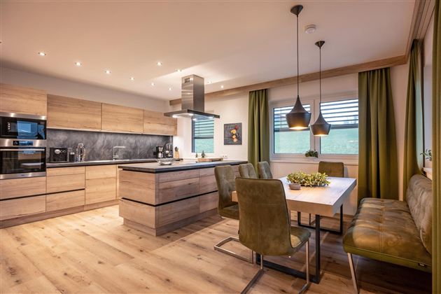 A modern kitchen with wooden surfaces and a cooking island. The dining area is cozy with a wooden table and green chairs.