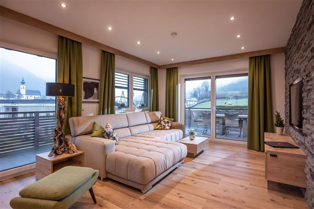 A modern living room with a large couch and a cozy armchair. Large windows offer a view of the landscape.