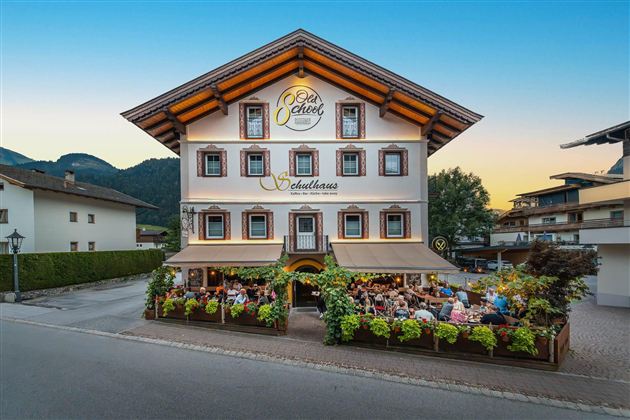 A charming restaurant with a blooming terrace and an inviting ambiance. The facade of the house is traditionally designed and surrounded by mountains.