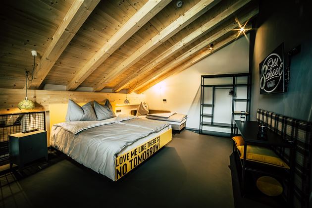 A modern bedroom with wooden ceilings and stylish furnishings. There is a large bed with creative bedding and a cozy seating area.