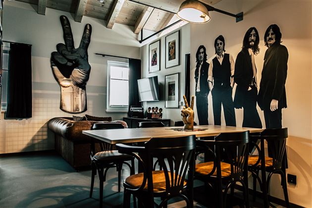 A stylish living and dining room with modern furniture. Large artistic graphics of people and a hand gesture for peace hang on the walls.