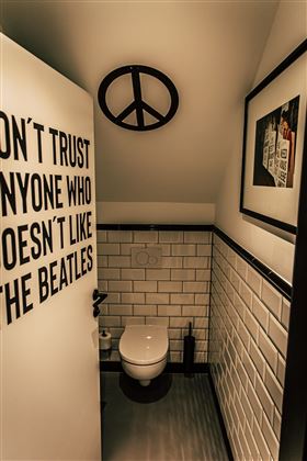 A modern bathroom with white tiles and a minimalist design. A sign on the wall alludes to the Beatles.