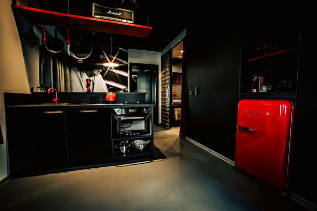A modern kitchen with black furniture and a red refrigerator. The environment is stylish and well-furnished.