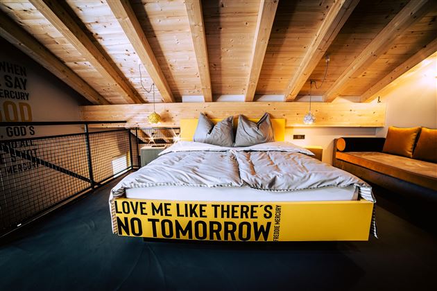 Ein modernes Schlafzimmer mit einem gemütlichen Bett und Holzdecke. Die Bettkante ist mit einer auffälligen Aufschrift versehen.