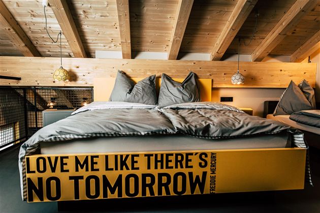 A modern bedroom with a striking bed and cozy bedding. The walls are made of wood, and the ceiling has exposed beams.