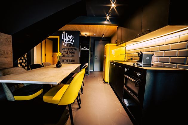 Eine moderne Küche mit schwarzen Schränken und einem gelben Kühlschrank. Der Essbereich hat einen großen Tisch und stylische Stühle.