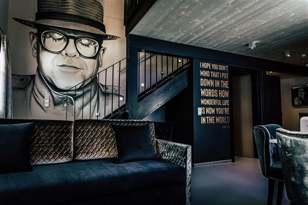 A modern living room with an artistic mural of a man. One wall features inspirational writings, while stylish furniture decorates the space.