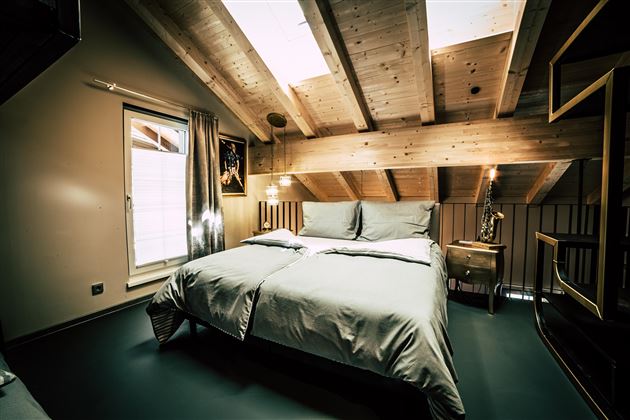 Ein modernes Schlafzimmer mit einem Doppelbett und Holzdecke. Große Fenster sorgen für viel Tageslicht.
