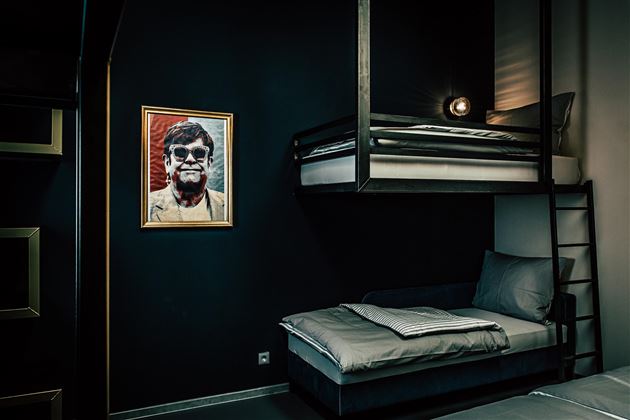 A modern room with dark walls and two beds. A striking artwork of a person hangs on the wall.