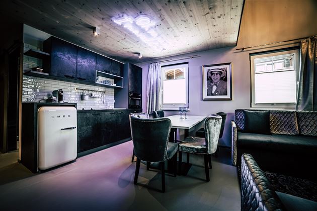 Eine moderne Küche mit dunklen Schränken und einem weißen Kühlschrank. Der gemütliche Essbereich hat elegante Stühle und große Fenster, die viel Licht einlassen.