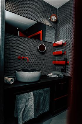 A modern bathroom with gray walls and red accents. In the foreground is a stylish sink and towels are neatly placed.